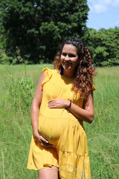 Foto jovem grávida no terceiro trimestre em um dia segurando sua barriga em um campo verde