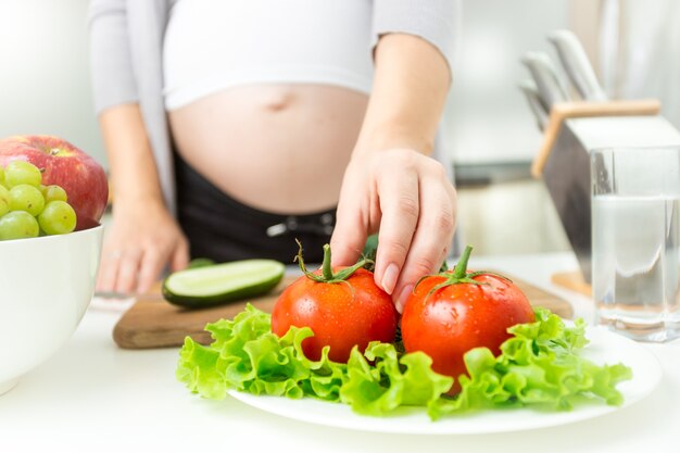 Jovem grávida pegando tomate fresco do prato