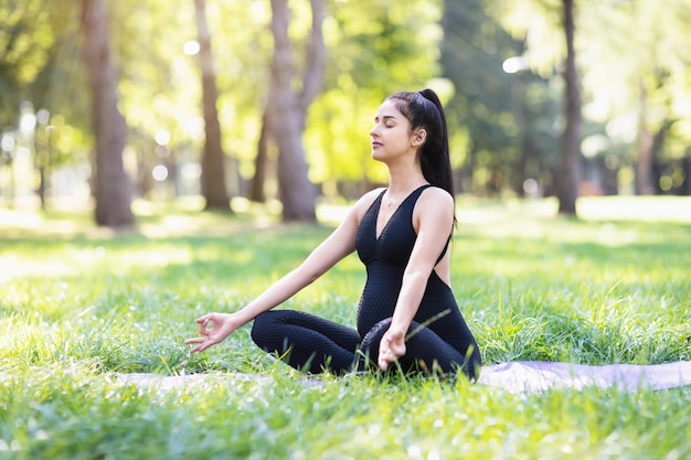 jovem grávida praticando ioga realiza meditação enquanto está sentado em uma posição de lótus