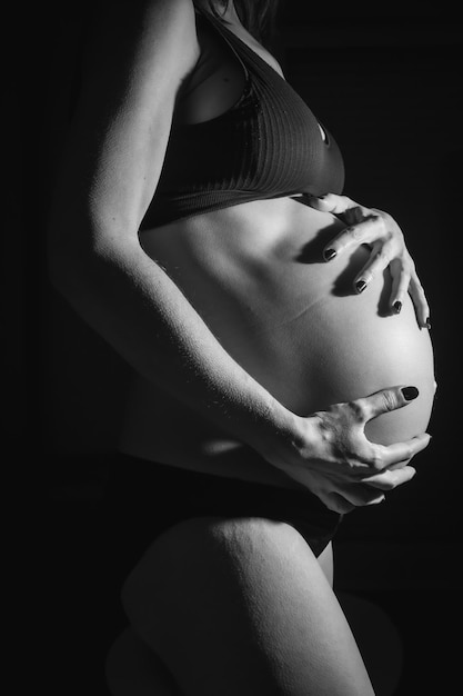 Jovem grávida prestes a dar à luz Com as mãos na barriga Em algumas fotos de estúdio fotos em preto e branco