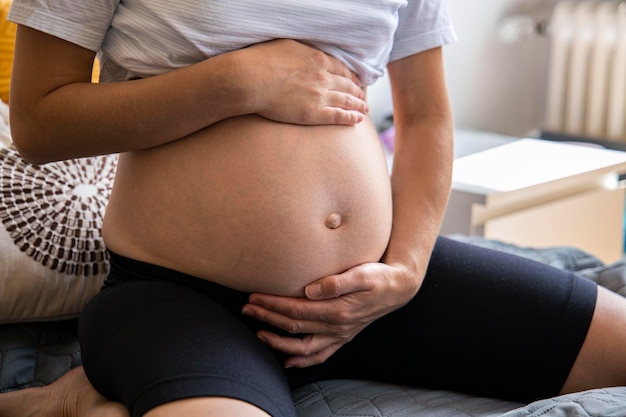 Jovem grávida segurando a barriga enquanto está sentada no sofá