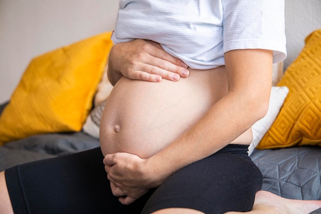 Foto jovem grávida segurando a barriga enquanto está sentada no sofá