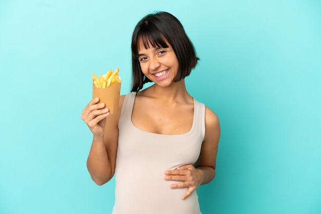 Jovem grávida segurando batatas fritas sobre fundo azul isolado