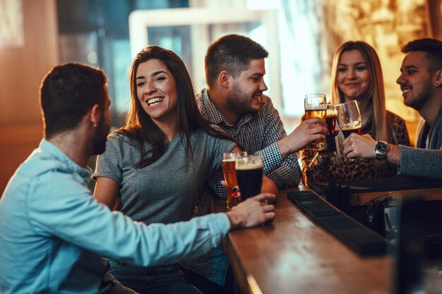 Jovem grupo de amigos está bebendo cerveja, conversando e se divertindo em um café.