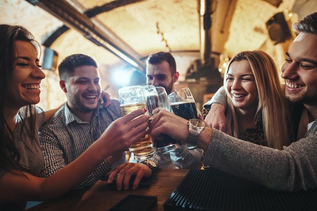 Jovem grupo de amigos está bebendo cerveja, conversando e se divertindo em um café.