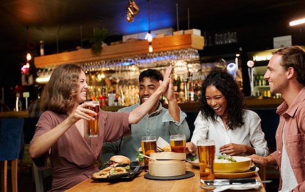 Jovem grupo multirracial de amigos em roupas casuais celebrando com comida e bebidas em um restaurante