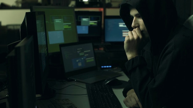 Jovem hacker profissional trabalhando em um escritório escuro com computadores de segurança cibernética e conceito de hacking
