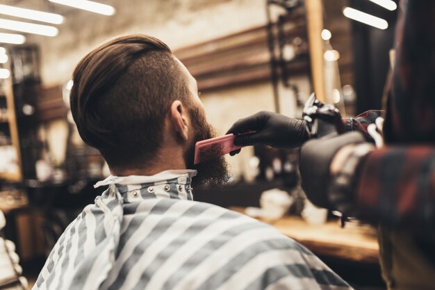 Jovem hippie bonito visitando a barbearia. corte e estilo de barba moderno e elegante.