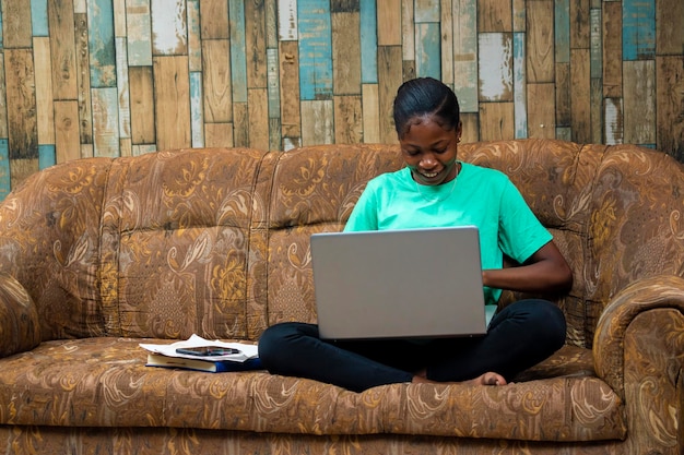 Jovem hipster africana negra trabalhando em casa sentada em um sofá usando computador portátil mulher de negócios comprando on-line em casa