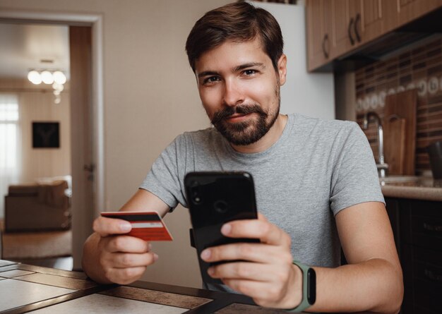 Jovem hipster compras on-line com cartão de crédito usando telefone inteligente em casa