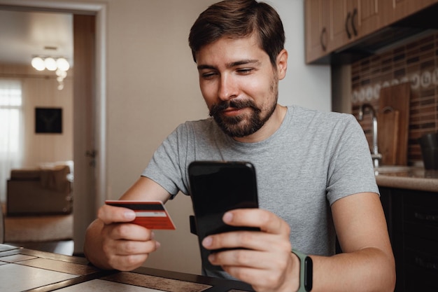 Jovem hipster compras on-line com cartão de crédito usando telefone inteligente em casa