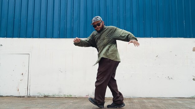 Jovem hipster dançando bboy passo de pé na rua com parede azul Endeavour