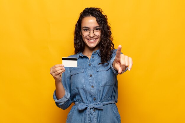 Jovem hispânica apontando com um sorriso satisfeito, confiante e amigável, escolhendo você