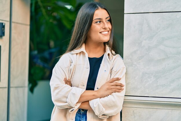 Jovem hispânica com braços cruzados sorrindo feliz na cidade