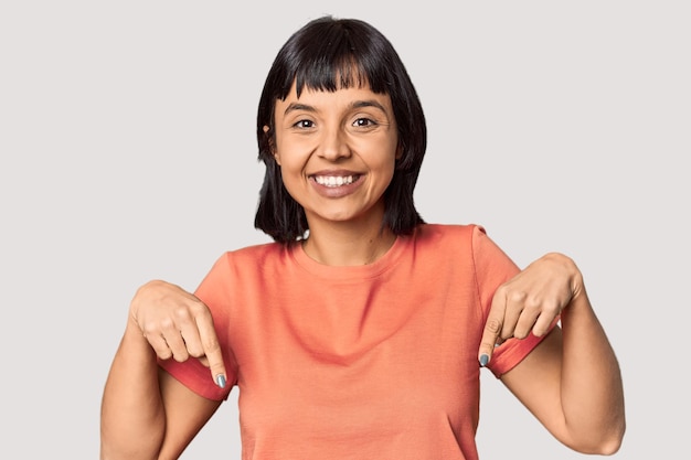 Foto jovem hispânica com cabelo preto curto no estúdio aponta para baixo com os dedos sentimento positivo