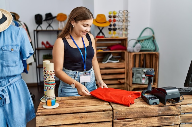 Jovem hispânica dobrando camiseta trabalhando em loja de roupas