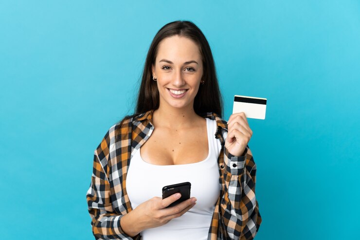 Foto jovem hispânica em um fundo azul isolado, comprando com o celular com um cartão de crédito
