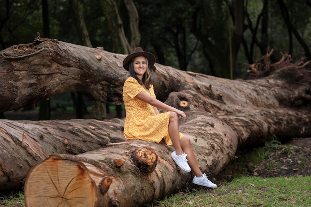 Jovem hispânica em um vestido amarelo sentado em um grande tronco de árvore em um parque