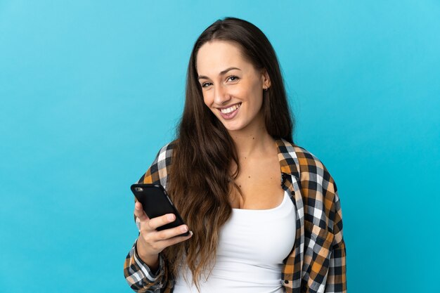 Jovem hispânica em uma parede azul isolada usando telefone celular