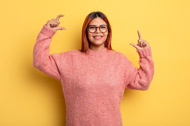 Foto jovem hispânica emoldurando ou delineando seu próprio sorriso com as duas mãos, parecendo positiva e feliz, conceito de bem-estar