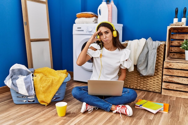 Foto jovem hispânica estudando enquanto espera a lavanderia preocupada e estressada com um problema com a mão na testa nervosa e ansiosa por crise