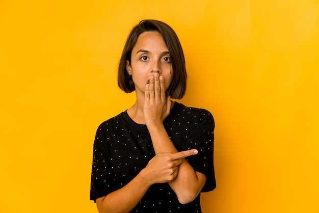 Foto jovem hispânica isolada em amarelo apontando para o lado