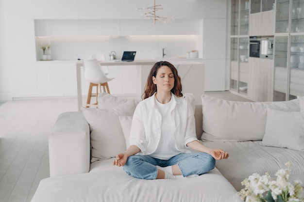 Jovem hispânica na prática de ioga e meditação no sofá em casa Zen encontrando