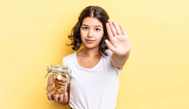 jovem hispânica olhando sério mostrando a palma da mão aberta, fazendo o gesto de parada. conceito de garrafa de biscoitos