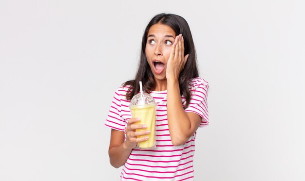 Jovem hispânica se sentindo feliz, animada e surpresa, segurando um milk-shake de baunilha