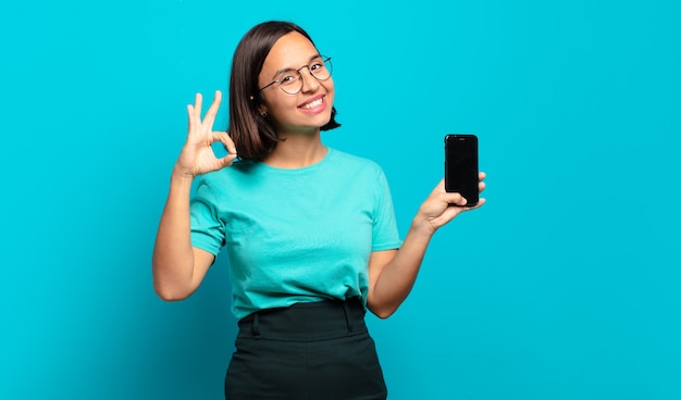 Jovem hispânica se sentindo feliz, relaxada e satisfeita, mostrando aprovação com um gesto de ok, sorrindo