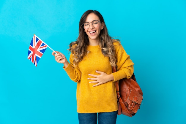 Jovem hispânica segurando uma bandeira do Reino Unido isolada no espaço azul e sorrindo muito
