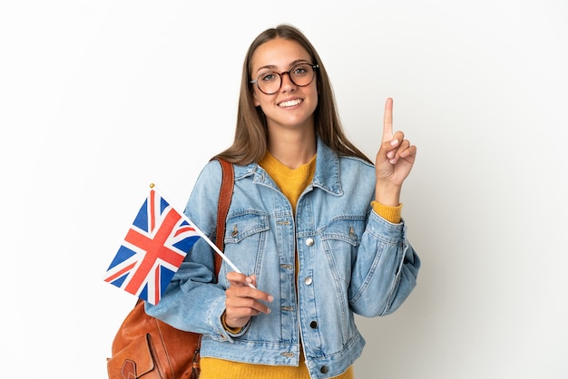 Jovem hispânica segurando uma bandeira do reino unido sobre um fundo branco isolado, mostrando e levantando um dedo em sinal dos melhores