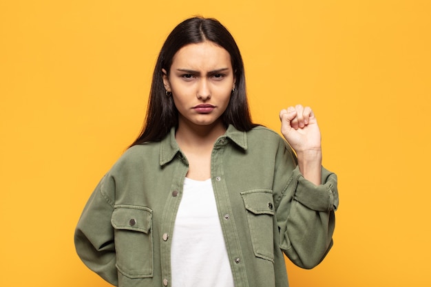 Jovem hispânica sentindo-se séria, forte e rebelde, levantando o punho, protestando ou lutando pela revolução