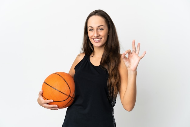 Jovem hispânica sobre fundo branco isolado jogando basquete e fazendo sinal de OK