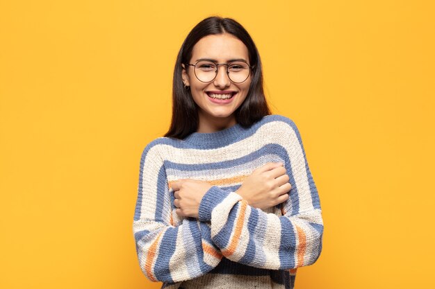 Jovem hispânica sorrindo alegremente e comemorando, com os punhos cerrados e os braços cruzados, sentindo-se feliz e positiva