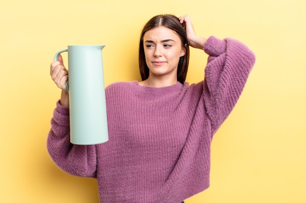 Jovem hispânica sorrindo alegremente e sonhando acordada ou duvidando. conceito de garrafa térmica de café