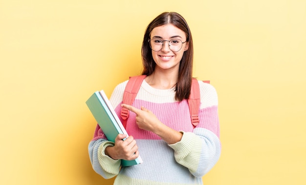 Jovem hispânica sorrindo alegremente, sentindo-se feliz e apontando para o lado. conceito de estudante