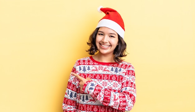 Jovem hispânica sorrindo alegremente, sentindo-se feliz e apontando para o lado. conceito de natal