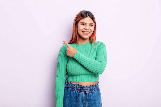 Jovem hispânica sorrindo alegremente, sentindo-se feliz e apontando para os lados e para cima, mostrando o objeto no espaço da cópia