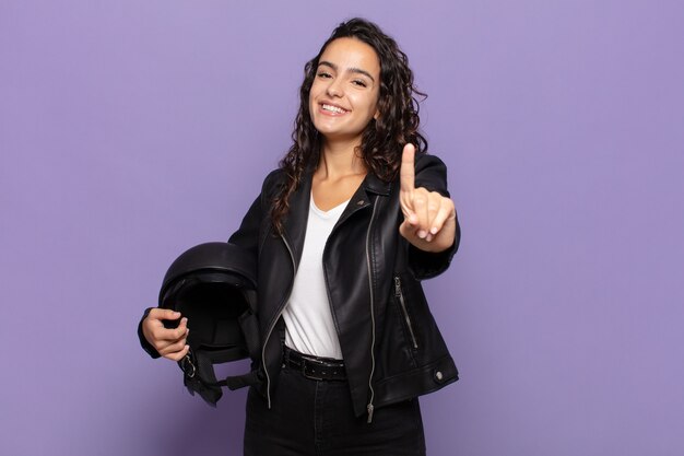 Jovem hispânica sorrindo com orgulho e confiança fazendo a pose número um triunfantemente, sentindo-se uma líder