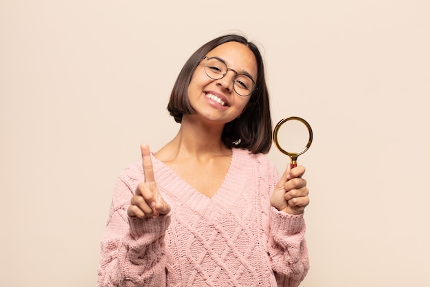 Jovem hispânica sorrindo com orgulho e confiança fazendo a pose número um triunfantemente, sentindo-se uma líder