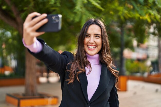 Jovem hispânica sorrindo confiante faz selfie pelo smartphone no parque