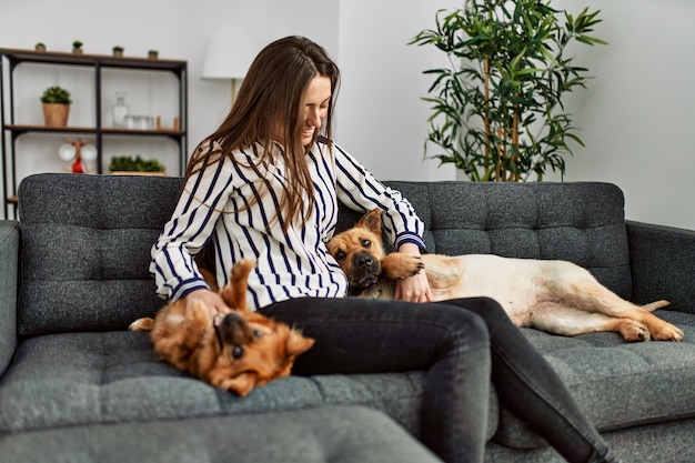 Jovem hispânica sorrindo confiante sentado no sofá com cachorros em casa