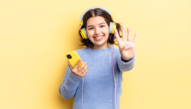 Jovem hispânica sorrindo e parecendo amigável, mostrando o número quatro. conceito de fones de ouvido e smartphone