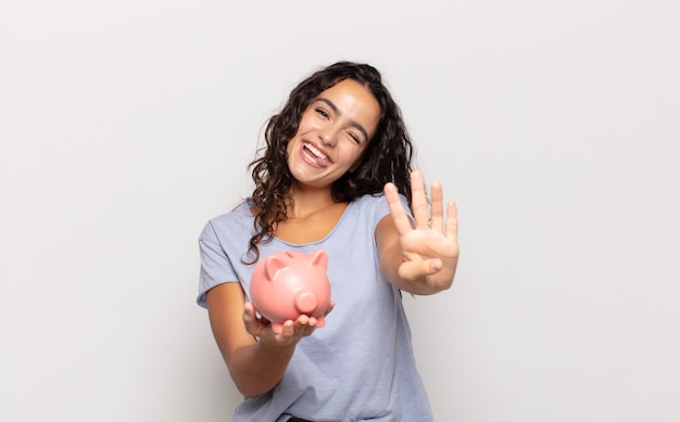 Jovem hispânica sorrindo e parecendo amigável, mostrando o número quatro ou o quarto com a mão para a frente