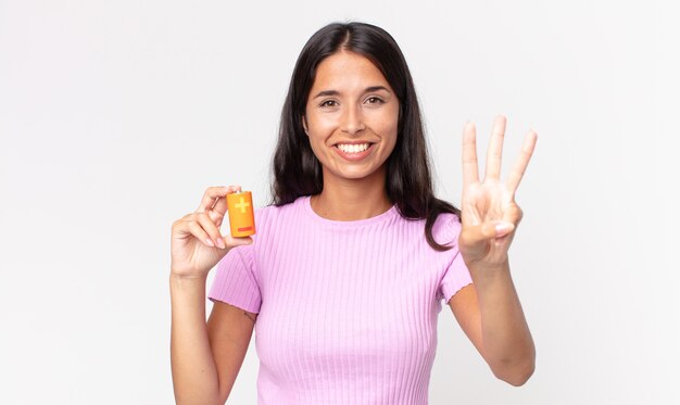 Jovem hispânica sorrindo e parecendo amigável, mostrando o número três e segurando baterias