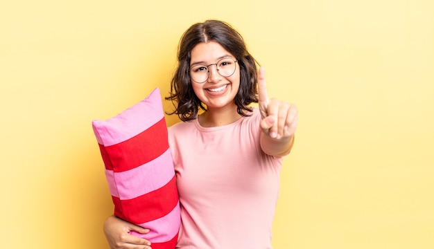 Jovem hispânica sorrindo e parecendo amigável, mostrando o número um. conceito de acordar de manhã