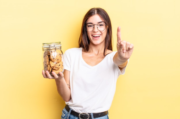 jovem hispânica sorrindo e parecendo amigável, mostrando o número um. conceito de garrafa de biscoitos