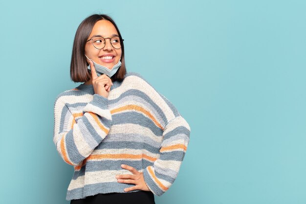 Jovem hispânica sorrindo feliz e sonhando acordada ou duvidando, olhando para o lado