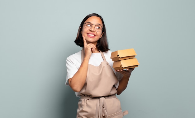 Jovem hispânica sorrindo feliz e sonhando acordada ou duvidando, olhando para o lado